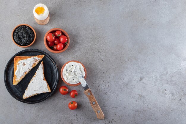 Toast con burro e pomodorini rossi posti su fondo in marmo.