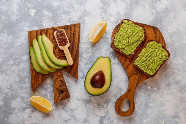 Toast di avocado aperto con fette di avocado, limone, semi di lino, semi di sesamo, fette di pane nero, vista dall'alto