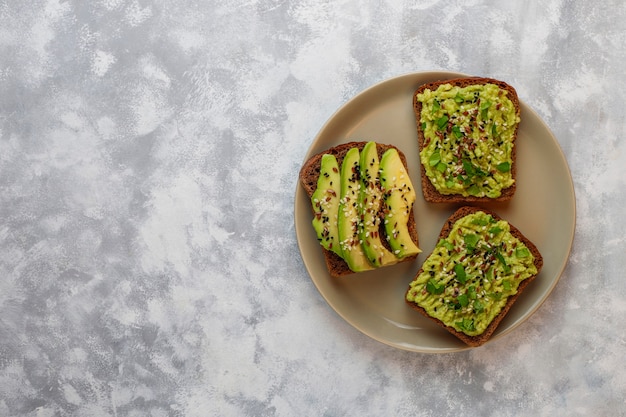 Toast di avocado aperto con fette di avocado, limone, semi di lino, semi di sesamo, fette di pane nero, vista dall'alto