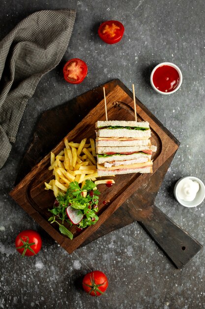 Top club sandwich con verdure patatine fritte e salse su legno ampio