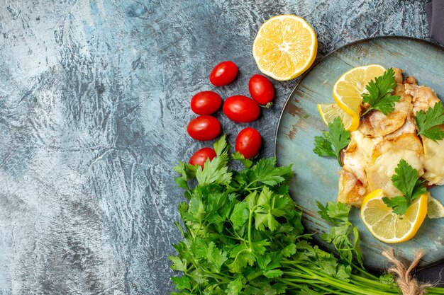 Top vista metà pollo con formaggio sul piatto mazzo di prezzemolo mezzo limone pomodorini sul tavolo grigio copia posto