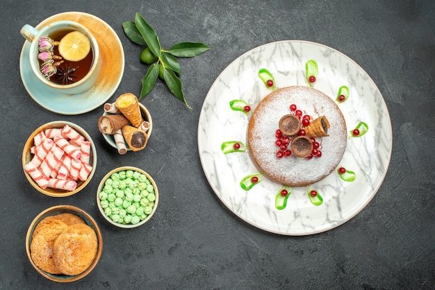 Top vista ravvicinata dolci una tazza di tè biscotti cialde caramelle agrumi torta con frutti di bosco