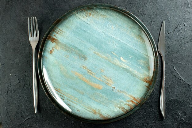 Top vista ravvicinata piatto rotondo cena coltello e forchetta sulla tavola nera