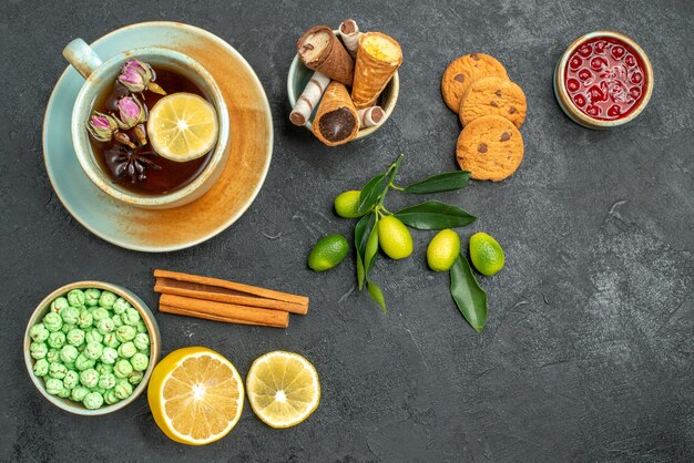 Top vista ravvicinata una tazza di tè una tazza di tè caramelle limone cannella marmellata agrumi biscotti