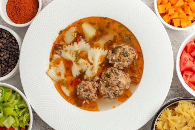 Top vista ravvicinata zuppa con carne deliziosa zuppa con verdure a fette e diversi condimenti sulla superficie bianca