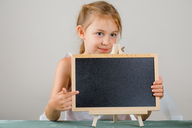 Torna al concetto di scuola vista laterale. bambina che tiene e che mostra lavagna.