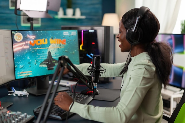 Torneo di videogiochi sparatutto spaziale vincente donna pro gamer che parla con i giocatori utilizzando il microfono durante lo streaming live, vincitore di successo che gioca ai videogiochi online utilizzando il computer RGB