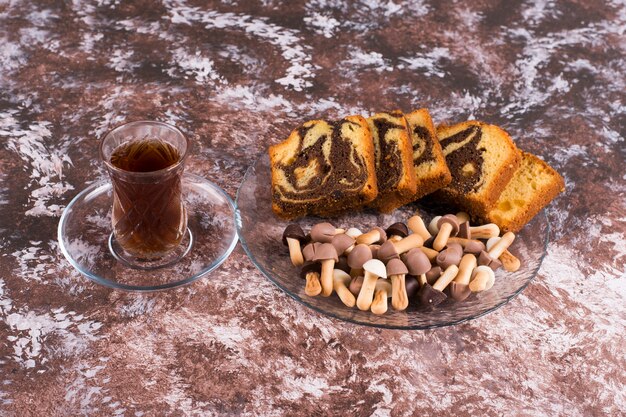 Torta al cacao con cialde e biscotti in un piatto di vetro con un bicchiere di tè