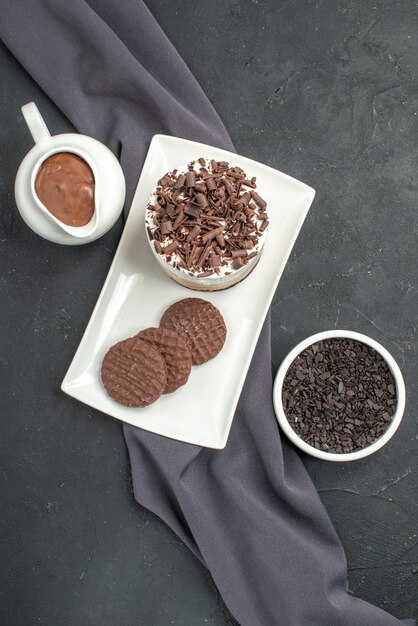 Torta al cioccolato e biscotti vista dall'alto su ciotole rettangolari bianche con scialle viola al cioccolato su sfondo scuro isolato