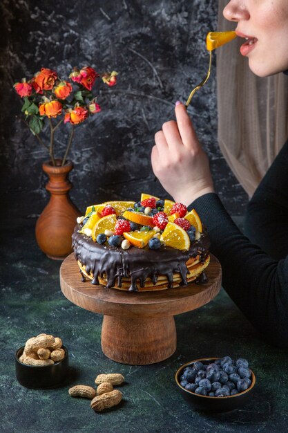 Torta al cioccolato squisita vista frontale con frutta fresca che viene mangiata dalla donna sulla parete scura