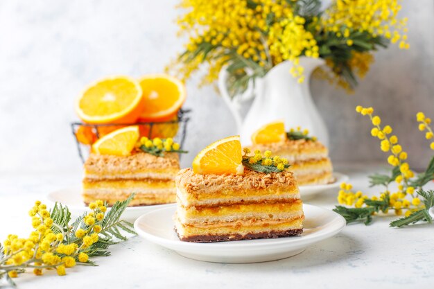 Torta arancione decorata con fette d'arancia fresche e fiori di mimosa sulla luce