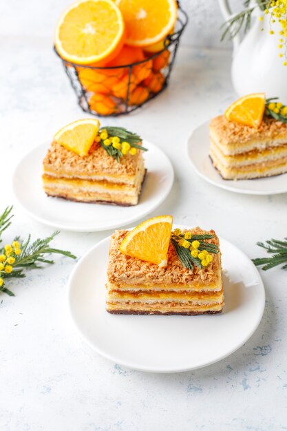 Torta arancione decorata con fette d'arancia fresche e fiori di mimosa sulla luce