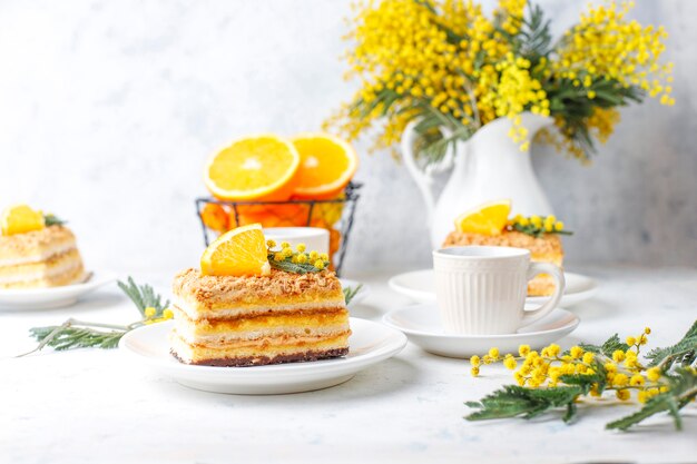 Torta arancione decorata con fette d'arancia fresche e fiori di mimosa sulla luce