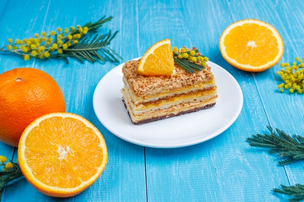 Torta arancione decorata con fette d'arancia fresche e fiori di mimosa sulla luce