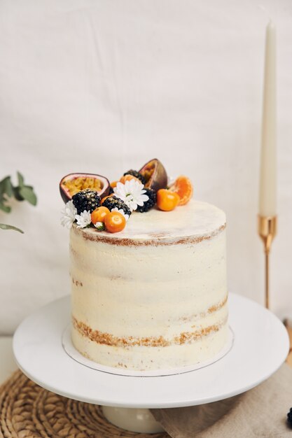 Torta bianca con frutti di bosco e frutti della passione accanto a una pianta dietro un bianco