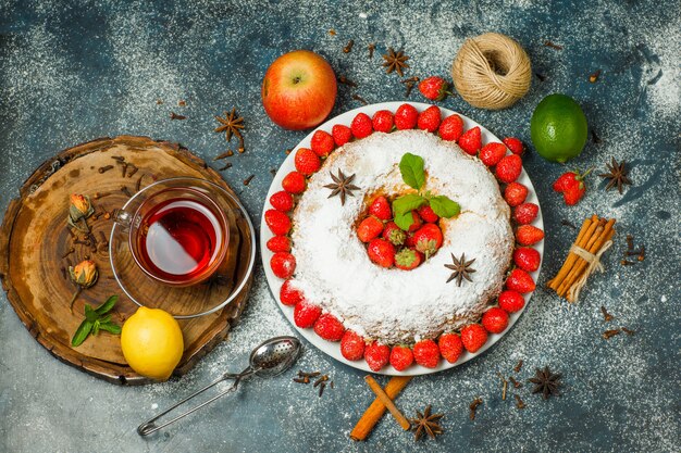 Torta con frutta, colino, tè, filo, spezie, zucchero, erbe aromatiche in un piatto su tavola di legno e sfondo di stucco, vista dall'alto.