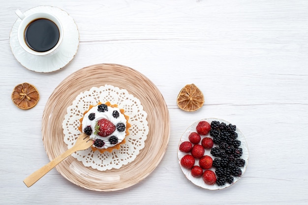 Torta cremosa gustosa vista dall'alto con frutti di bosco insieme a una tazza di bacche di caffè sulla bacca di colore dolce torta leggera scrivania