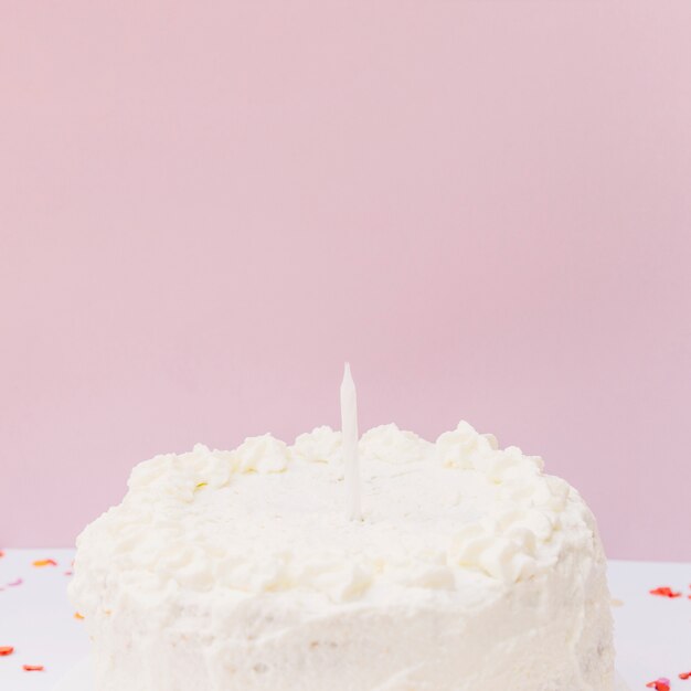 Torta di compleanno bianca con singola candela su sfondo rosa