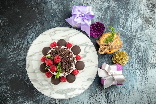 Torta di formaggio di vista superiore con i regali di natale dei biscotti legati piatto ovale al cioccolato sulla superficie grigia