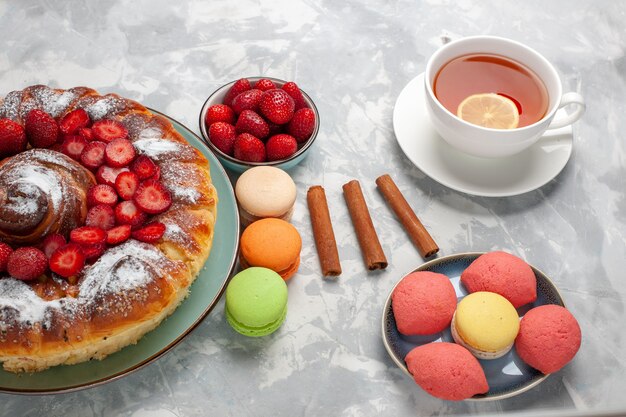 Torta di fragole gustosa con zucchero a velo e macarons e tè sulla superficie bianca