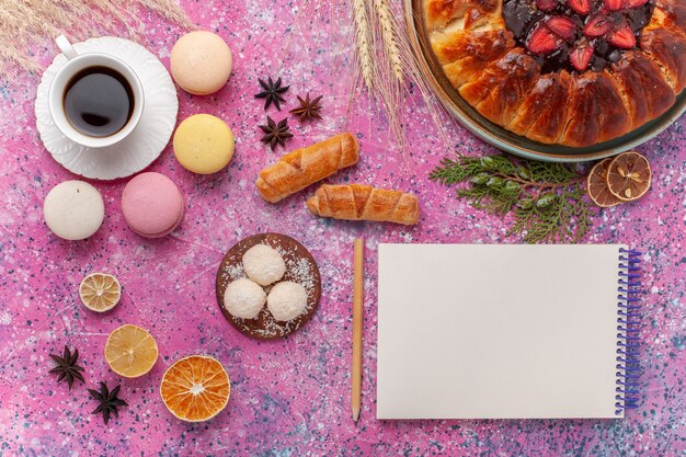 Torta di fragole squisita vista dall'alto con una tazza di tè e macarons sul rosa