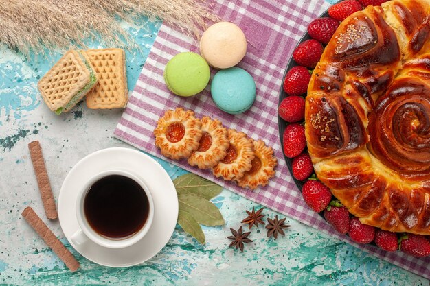 Torta di fragole vista dall'alto con una tazza di biscotti da tè e macarons francesi sulla superficie blu