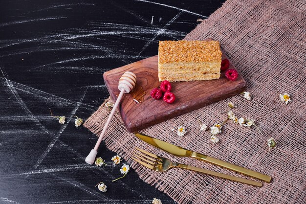 Torta di miele con cucchiaio di miele e lamponi su sfondo scuro.