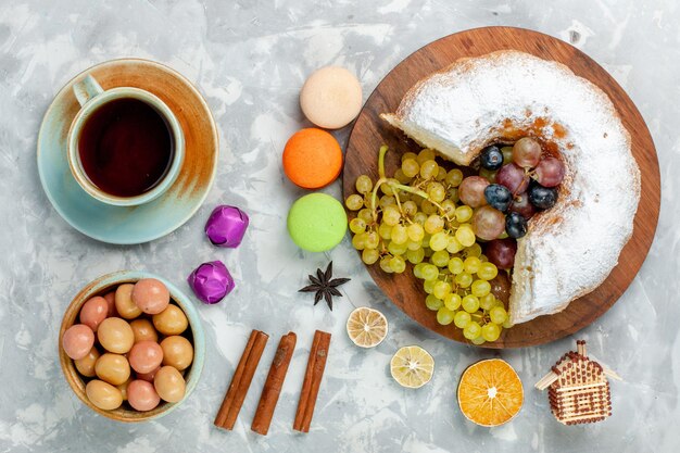 Torta in polvere vista dall'alto con tè all'uva fresca e macarons francesi sulla scrivania bianca