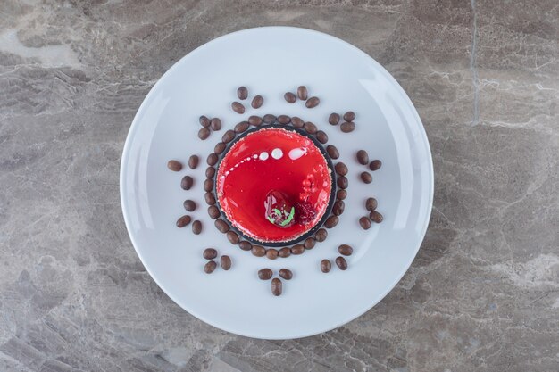 Torta piccola, con copertura di sciroppo di fragole e chicchi di caffè su un piatto da portata su superficie di marmo