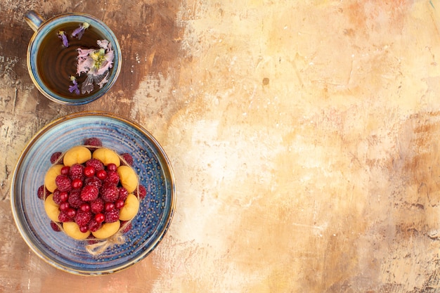 Torta regalo appena sfornata con frutta su un vassoio blu e una tazza di tè sulla tavola di colori misti