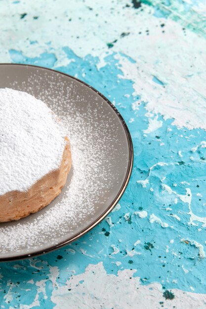 Torta rotonda vista frontale con polvere di zucchero all'interno della piastra sulla superficie azzurra torta cuocere biscotti zucchero colore tè dolce
