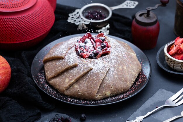 Torta vegana cruda fresca con frutti di bosco su un vassoio nero