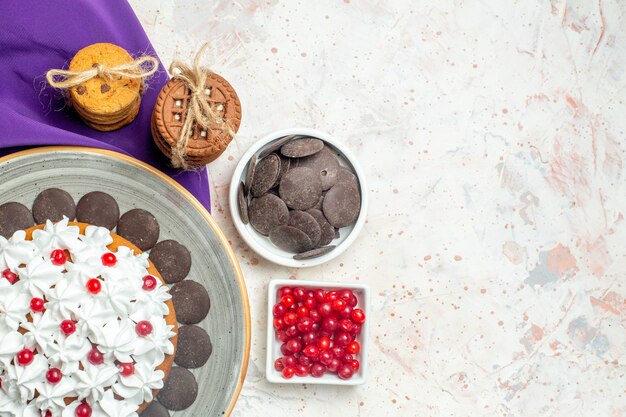 Torta vista dall'alto con crema pasticcera su piatto ovale biscotti a scialle viola legati con corda cioccolato e frutti di bosco in ciotole