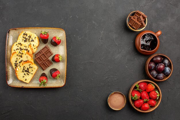 Torta vista dall'alto e pezzi di torta alle fragole con cioccolato a sinistra e ciotole con bacche di fragole e salsa al cioccolato sul lato destro del tavolo