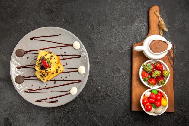 Torta vista dall'alto e torta ai frutti di bosco con cioccolato e fragole sul piatto accanto al tagliere con ciotole di dolci e fragole in salsa di cioccolato