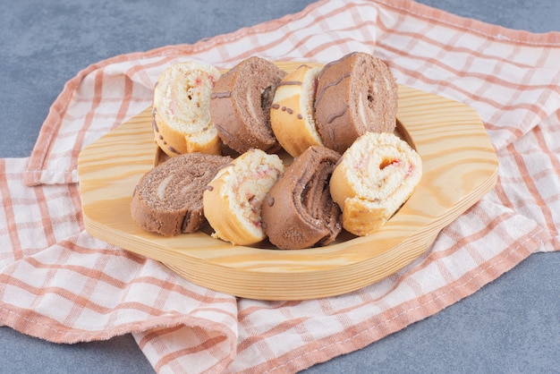 Torte di rotolo a fette nel bordo, sul tovagliolo sullo sfondo di marmo.