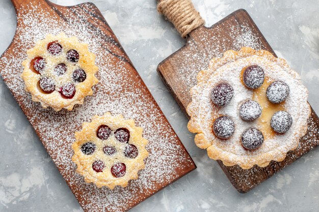 Torte in polvere di zucchero di vista superiore con frutta sulla frutta dolce dello zucchero del biscotto della torta grigia della scrivania