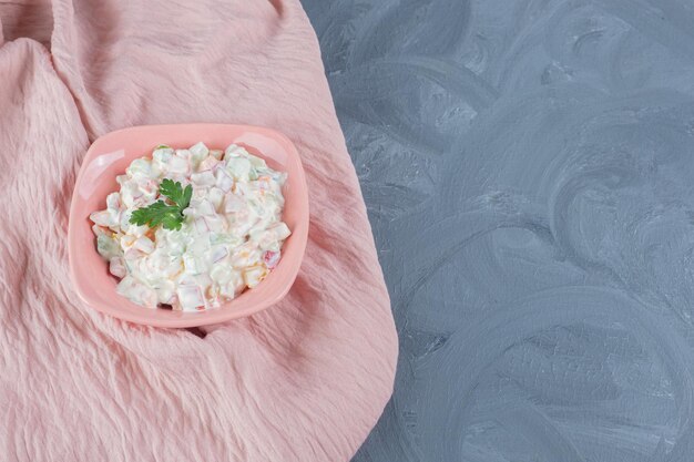 Tovaglia rosa sotto una ciotola di insalata olivier su sfondo marmo.