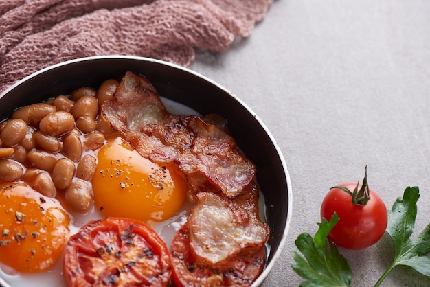 Tradizionale colazione inglese completa in padella con uova fritte, pancetta, fagioli, pomodori grigliati.