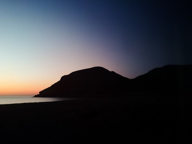 Tramonto con una montagna di sagoma sulla spiaggia