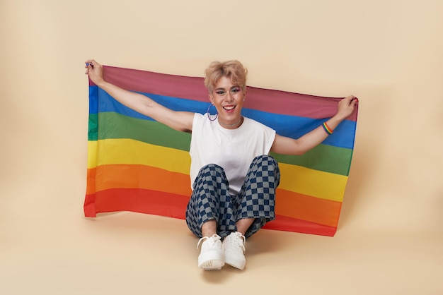 Transgender asiatico giovanile LGBT con bandiera arcobaleno sulla spalla isolata su sfondo color nudo