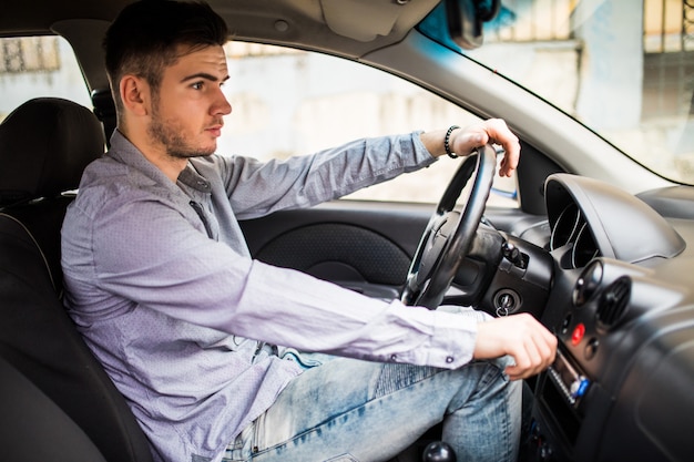 Trasporti, viaggi d'affari, tecnologia e concetto di persone. Giovane in tuta guida auto e regolazione del volume della musica sul sistema stereo del pannello di controllo