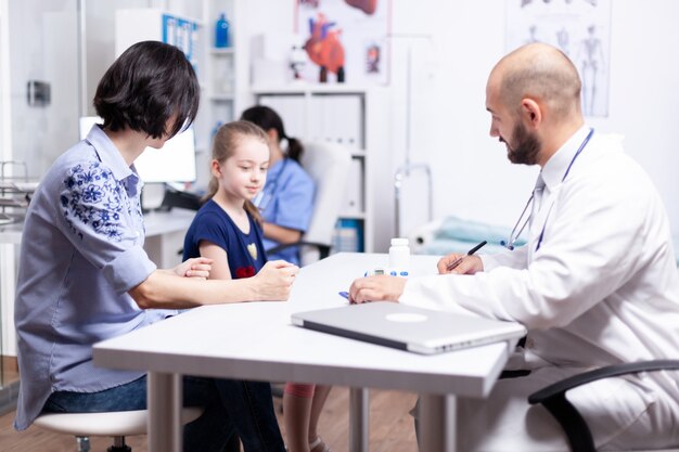 Trattamento di scrittura del pediatra dopo la consultazione del bambino malato nell'ufficio dell'ospedale. Medico sanitario specialista in medicina che fornisce servizi di assistenza sanitaria esame di trattamento.