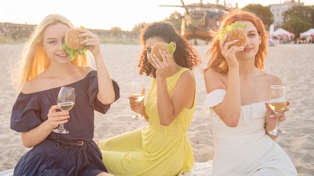 Tre amiche che godono di hamburger in spiaggia