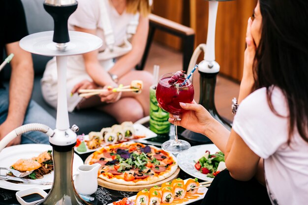 Tre amici a cena con insalata di pizza sushi e narghilè