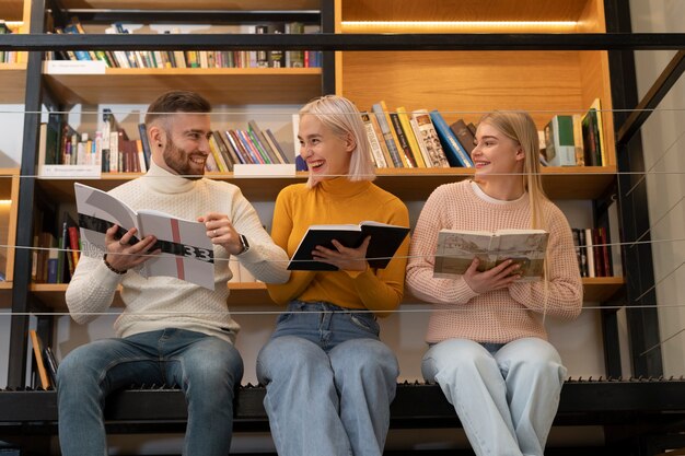 Tre amici che leggono dai libri e da un taccuino in una biblioteca