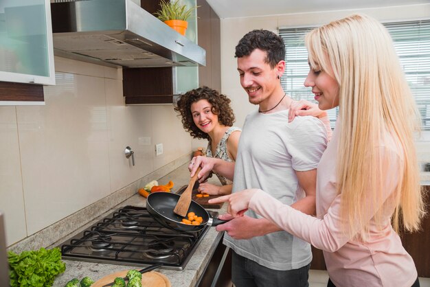 Tre amici che si divertono mentre cucinano il cibo nella padella