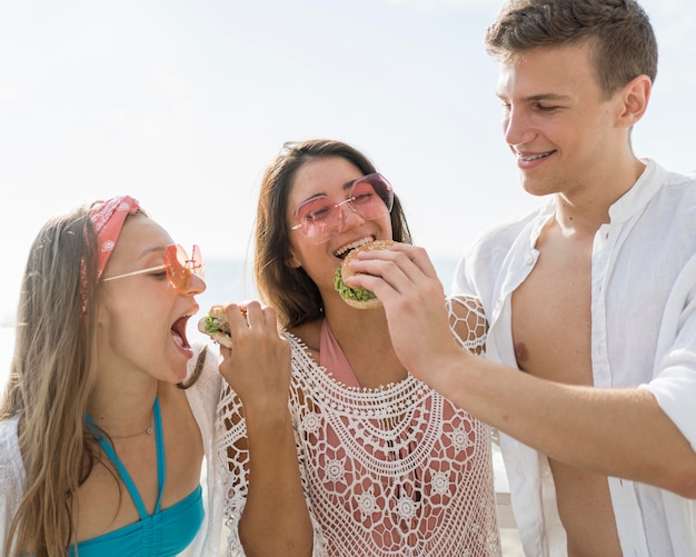 Tre amici felici all'aperto che mangiano hamburger insieme