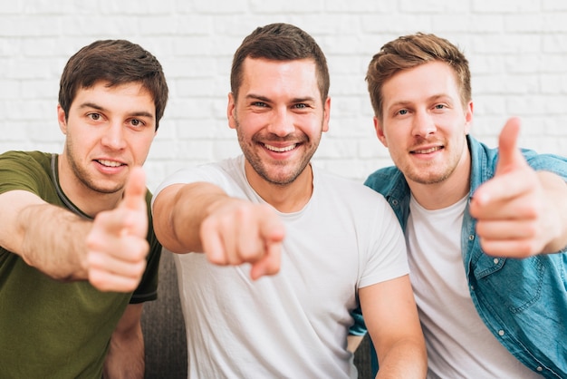 Tre amici maschi felici che indicano dito verso la macchina fotografica