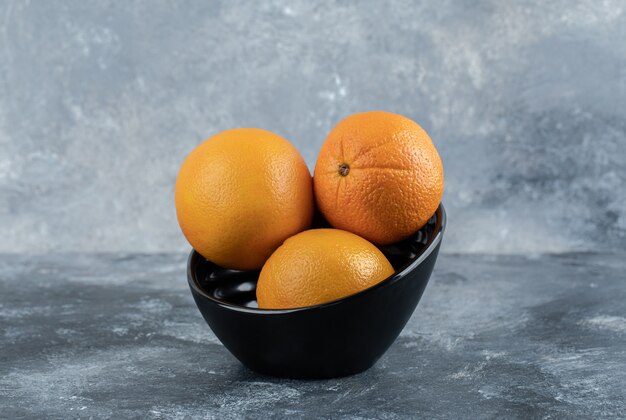 Tre arance fresche in una ciotola nera.